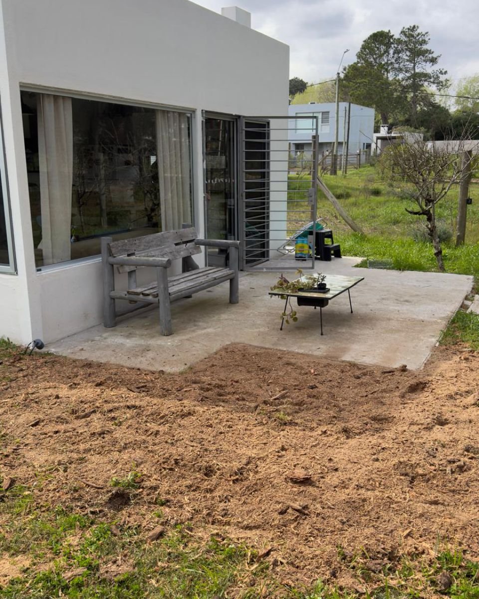 Tierra nivelada junto a la terraza de hormigón de una casa después de fresar el tocón y sus raíces